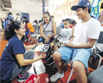  ?? JOHN MAHONEY ?? Volunteer Aura Perez brings shoes to Carlos Del Valle, right, with his brother Rodrigo and mother Ann Lesly Altamirano, at the Welcome Hall Mission on Tuesday. The mission is helping families prepare for their children’s return to school next month.