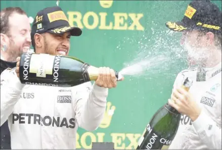  ?? MIGUEL SCHINCARIO­L/AFP ?? Brazilian Grand Prix winner Lewis Hamilton (left) sprays champagne in the face of title rival and Mercedes teammate Nico Rosberg as they celebrate on the podium at Interlagos on Sunday.