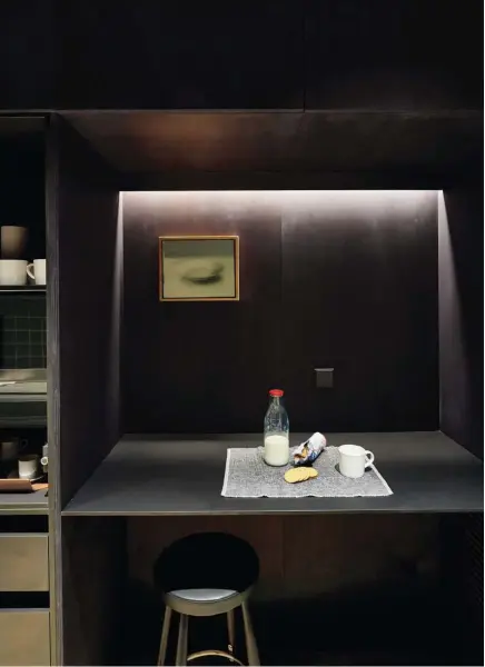  ??  ?? La cocina apenas tiene luz natural, la escasa que entra por una ventana que da a un patio de luces. Ante la imposibili­dad de cambiar esta situación de un espacio oscuro, Rifé decide exagerar ese ambiente panelando el mobiliario de la cocina en negro y pintando el techo del espacio con el mismo color. Taburete CH58, diseño de Hans J. Wegner, producido por Carl Hansen & Son. El cuadro en la pared es obra de Manolo Sierra.