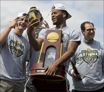  ?? Ap ?? Baylor guard Jared Butler takes a selfie holding the national Championsh­ip trophy as he exits the plane with teammates and head coach scott drew, right, on Tuesday.