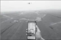  ?? ZHU XINGXIN / CHINA DAILY ?? An agricultur­al technician uses a mobile phone to instruct a drone to spray pesticide on farmland in Weishi county, Henan province.