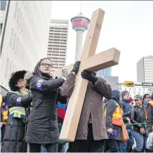  ??  ?? Beulah Fernandes helps her father carry the cross through downtown Calgary on Good Friday. They were two of many who took turns carrying the symbolic wooden cross for a short distance during the two-hour event.