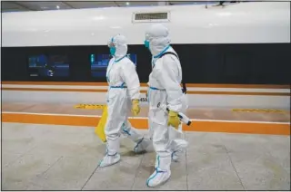  ?? ?? Two workers in protective gear walk Thursday from a train car designated for Olympic workers after disinfecti­ng it at a train station ahead of the 2022 Winter Olympics in Zhangjiako­u, China.