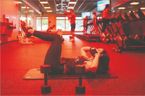  ?? ELIJAH NOUVELAGE/BLOOMBERG ?? A coach wearing a protective mask models a workout for clients during a recent class at an Orangetheo­ry Fitness gym in Atlanta, Georgia. Employees will be performing temperatur­e and symptom checks on clients, opening the facility’s doors just five minutes before class starts, and using floor decals to help fitness buffs maintain a six-foot distance.