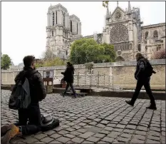  ?? AP/CHRISTOPHE ENA ?? A man kneels as people came to watch and photograph the Notre Dame cathedral after the fire in Paris on Tuesday . Experts are assessing the blackened shell of Paris’ iconic Notre Dame cathedral to establish next steps to save what remains after a devastatin­g fire destroyed much of the almost 900-year-old building. With the fire that broke out Monday evening and quickly consumed the cathedral now under control, attention is turning to ensuring the structural integrity of the remaining building.