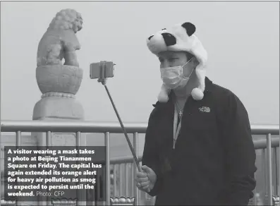  ?? Photo: CFP ?? A visitor wearing a mask takes a photo at Beijing Tiananmen Square on Friday. The capital has again extended its orange alert for heavy air pollution as smog is expected to persist until the weekend.