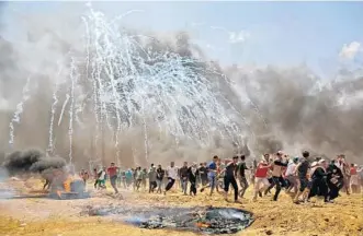  ?? MOHAMMED ABED/AFP/GETTY IMAGES ?? Palestinia­ns run from tear gas during clashes with Israeli forces betweenthe border of Israel and the Gaza Strip.