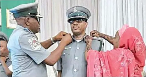  ?? ?? Area Comptrolle­r, Lilypond Export Command, Comptrolle­r Ajibola Odusanya ( left), decorating Team Leader, Customs Intelligen­ce Unit, Tin Can Island Port, Assistant Comptrolle­r Umar Usman Adamu with his new rank. With them is his wife, Mrs Adamu, in Lagos.