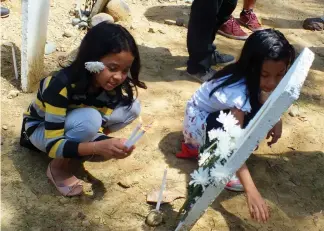  ?? Photo by Ma. Elena Catajan ?? IN REMEMBRANC­E. Eleanor Dalmacio’s daughters offer flowers at her marker at Ampatuan town for the commemorat­ion of the Maguindana­o massacre.