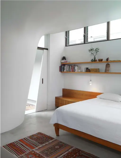  ??  ?? Bedroom Tranquil in all-white, with its diagonal sliding door and curved wall, this bedroom’s main focus is the bespoke shelving and a wooden bench with built-in storage. The pendant light, matching the one in the bathroom, was also purchased from Australian store Hub Furniture. A rug from Sydney-based The Rug Experts introduces warmth and colour Garden Perfect for entertaini­ng, this shady, landscaped space features a lap pool and an outdoor cooking area See Stockists page for details