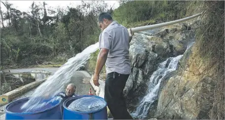  ?? Photograph­s by Carolyn Cole Los Angeles Times ?? LUIS HERNANDEZ, left, and Sergio Rivera fill drums with spring water in Jayuya, where the water system has not been fully restored.