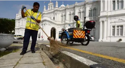  ??  ?? Satisfying work: Mohammad Zulfadli sweeping in front of the City Hall building at the Esplanade as other young MBPP workers clean a restroom near the food court along Gurney Drive in George Town.