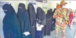  ?? AFP ?? A security personnel stands guard as voters stand in a queue , in Varanasi.