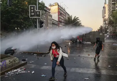  ?? FOTO: ESTEBAN FELIX/TT-AP ?? En regeringsk­ritisk demonstran­t tar sig bort från polisens vattenkano­n
■ i Santiago, Chile.