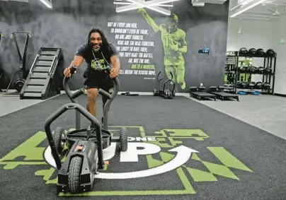  ?? KIM HAIRSTON/BALTIMORE SUN ?? Shel Simon, chief program officer of Next One Up, demonstrat­es a push sled in the new recreation­al center. The graphic features Terry Jones, a safety at Old Dominion, an alum of the program.