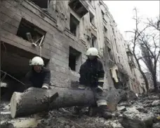 ?? Andrii Marienko/Associated Press ?? Emergency workers saw a tree in front of a residentia­l building, which was hit by a Russian rocket Sunday at the city center of Kharkiv, Ukraine.