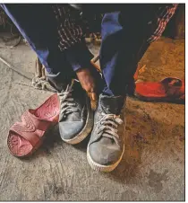  ??  ?? Imradul Ali puts on a pair of shoes which he salvaged from a landfill before going to school.