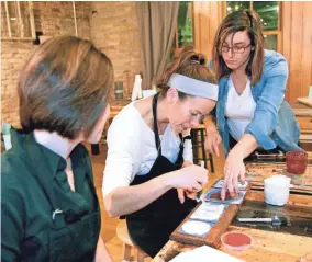  ?? PHOTOS BY ANGELA PETERSON/MILWAUKEE JOURNAL SENTINEL ?? Marianne Jones (center) works on plaque that spells out "home" with the state of Wisconsin shape in the place of the "o." Her neighbor and friend Sara North (left) and Pin-It Live co-owner Katie Garcia help her with her craft. See more at...