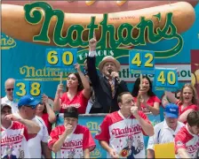  ??  ?? Master of Ceremony George Shea (top center) announces that reigning champion Joey Chestnut (bottom center) is winning the men’s competitio­n of the Nathan’s Famous Fourth of July hot dog eating contest in the final seconds of the competitio­n on Wednesday. AP PhoTo/MAry AlTAffer