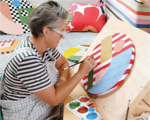  ??  ?? ABOVE / As well as being an award-winning interior designer, blogger, shop owner and mum, Alex is an artist, crafting precise freehand-painted works on fabric, canvas and board. Works which embrace her love of bold colour combinatio­ns. She is pictured here working in her home studio. Photo Julia Atkinson-Dunn.