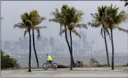  ?? LYNNE SLADKY — THE ASSOCIATED PRESS FILE ?? The Miami skyline is shrouded in clouds as a cyclist rides along Biscayne Bay at Matheson Hammock Park, May 15in Miami. National Oceanic and Atmospheri­c Administra­tion’s Climate Prediction Center, said that six to 10of the storms could develop into hurricanes.