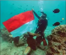  ?? JAWA POS PHOTO ?? ”PRASASTI TSUNAMI”: Wartawan Jawa Pos Eko Priyono mengibarka­n bendera Merah Putih di taman bawah laut Pulau Rubiah Senin lalu (14/8). Sepeda motor itu terbawa arus tsunami pada 2004 dan menjadi rumah karang.
