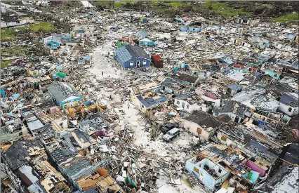  ?? Al Diiaz / Associated Press ?? People walk through a neighborho­od destroyed by Hurricane Dorian at Marsh Harbour in Great Abaco Island, Bahamas on Thursday.