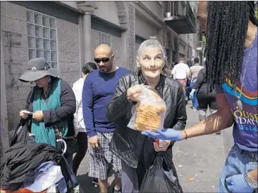  ?? Genaro Molina Los Angeles Times ?? KING JAMES, right, a volunteer with the My Friend’s House Foundation, gives bread to a homeless woman on skid row. The city’s DTLA 2040 plan proposes rezoning parts of the district for market-rate housing.