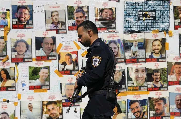  ?? BILD: ARIEL SCHALIT ?? En polis i Tel Aviv passerar en vägg med foton på Hamas gisslan. Bild från 26 februari.