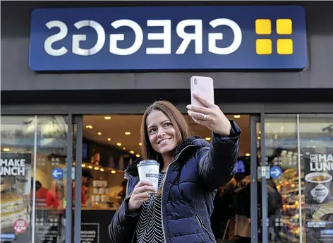  ??  ?? Customer Jennifer Cornell takes a selfie with the new backwards sign at Greggs bakery on Northumber­land Street in Newcastle-upon-Tyne. It has been created as a mirror image so it reads the correct way when reflected on the famous Fenwick Christmas window opposite