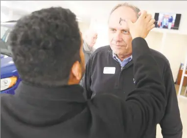  ?? Tyler Sizemore / Hearst Connecticu­t Media ?? Car salesman Miles Mobius receives ashes for Ash Wednesday at the Lincoln Ford dealership in Stamford.