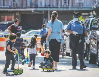  ?? BRENDAN MCDERMID / REUTERS FILES ?? A New York City police officer watches as children play while families wait in line at a food bank in Queens. A syndrome linked to COVID-19 in children has surfaced at Mount Sinai Kravis Children’s Hospital in New York.