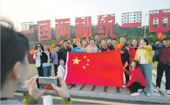  ?? ?? A group poses with a Chinese flag in front of a giant slogan which reads “One Country, Two Systems, Unify China”, which can be seen from Taiwan’s Kinmen Island, on the beach in Xiamen, in China’s southeast Fujian province. PHOTO: AFP