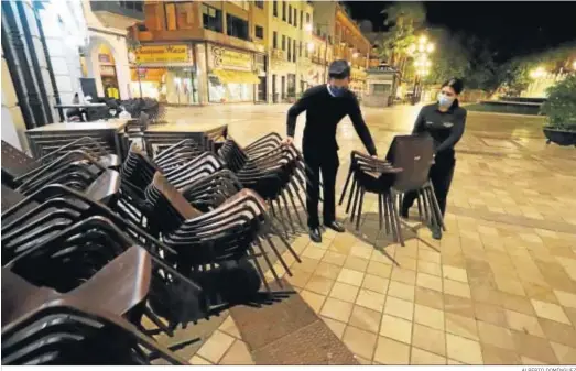  ?? ALBERTO DOMÍNGUEZ ?? Dos empleados de un bar de Huelva recogen las sillas de la terraza para cumplir con el horario de cierre por la pandemia.