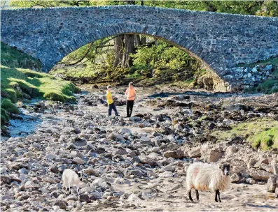  ??  ?? Bridge over vanished water: Children play on a dry river bed in Yockenthwa­ite, North Yorkshire