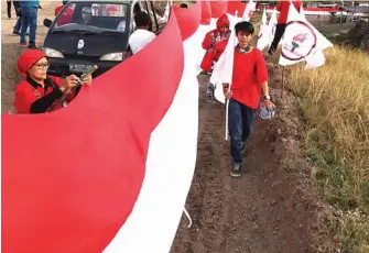  ?? FRIZAL/JAWA POS ?? BULAN BUNG KARNO: Anggota TMP dan Kader PDIP Sidoarjo membentang­kan bendera Merah Putih di tanggul lumpur kemarin.