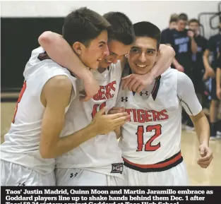  ??  ?? Taos' Justin Madrid, Quinn Moon and Martin Jaramillo embrace as Goddard players line up to shake hands behind them Dec. 1 after Taos' 58-34 victory against Goddard at Taos High School.