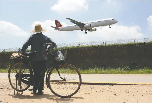  ?? STR / AFP / GETTY IMAGES ?? A farmer watches as a plane arriving from Taiwan lands at the airport in Xiamen, China. Taiwanese pilots have been following some of toughest COVID measures in the world and they say it’s affecting their mental health.