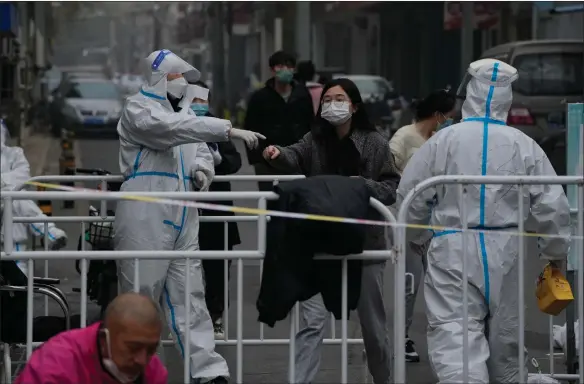  ?? Picture: Ap/andy Wong ?? A woman wearing a face mask on her way to collect her groceries as workers in protective suits stand guard in a locked-down neighborho­od as part of Covid-19 controls in Beijing. China is expanding lockdowns, including in a central city where factory workers clashed this week with police, as its number of Covid cases hit a daily record