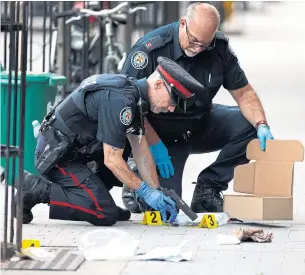  ?? COLE BURSTON PHOTOS THE CANADIAN PRESS ?? Police examine a gun found at the scene of a drive-by daylight shooting on Roncesvall­es Ave. Paolo Caputo, 64, of Richmond Hill, was killed at about 4 p.m. Friday outside Domani Restaurant.