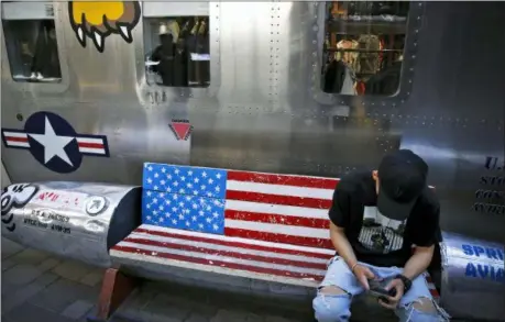  ?? ANDY WONG — THE ASSOCIATED PRESS ?? A man browses his smartphone on a bench with a decorated with U.S. flag outside a fashion boutique selling U.S. brand clothing at the capital city’s popular shopping mall in Beijing, Monday.