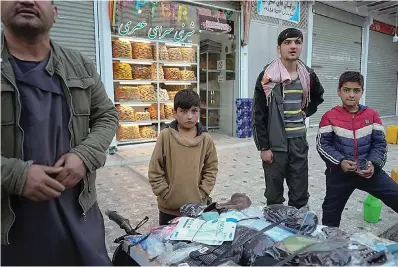  ?? AP Photo/Mstyslav Chernov ?? ■ Sanam — a bacha posh, a girl living as a boy— stands next to her father at their street stand selling masks Dec. 7, 2021, in Kabul, Afghanista­n. In the heavily patriarcha­l, male-dominated society of Afghanista­n, where women and girls are usually relegated to the home, there is one tradition which allows girls access to the male world: bacha posh. A girl dresses, behaves and is treated as a boy, allowing her to play and to work as a boy would be able to do, until she reaches puberty.