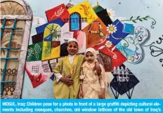  ?? — AFP ?? MOSUL, Iraq: Children pose for a photo in front of a large graffiti depicting cultural elements including mosques, churches, old window lattices of the old town of Iraq’s northern city of Mosul on the first night of the Muslim holy fasting month of Ramadan yesterday during a celebratio­n hosted by a local cultural NGO.