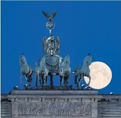  ?? REUTERS ?? An almost full moon is seen behind the quadriga statue atop the Brandenbur­g Gate in Berlin, Germany.