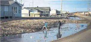  ?? NATHAN DENETTE THE CANADIAN PRESS FILE PHOTO ?? Indigenous children play in water-filled ditches in Attawapisk­at, Ont., in 2016. Community leaders say they feel “out of sight, out of mind” when it comes to improving infrastruc­ture.
