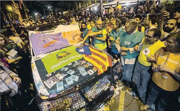  ?? QUIQUE GARCÍA / EFE ?? Un grupo de manifestan­tes observa uno de los vehículos dañados de la Guardia Civil en las protestas del día 20 frente al Departamen­t d’Economia