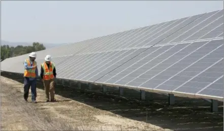  ?? RICH PEDRONCELL­I — THE ASSOCIATED PRESS FILE ?? Solar technician Joshua Valdez, left, and senior plant managerTim Wisdom walk past solar panels at a Pacific Gas and Electric Solar Plant in Dixon, California. Cheap solar panels imported from China and other countries have led to a boom in the U.S....