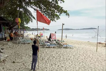  ?? — AP ?? Red for danger: A man raising a red flag indicating rough weather conditions in Chaweng beach, Koh Samui, as a tropical storm approaches.