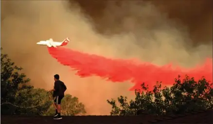  ?? WALLY SKALIJ, TNS ?? A.J. Moberg, 15, waters down the roof of his family’s house and a plane drops fire retardant as a wildfire approaches in Santa Clarita, Calif.