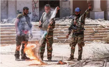  ??  ?? Syrian government soldiers burn an opposition flag while flashing the victory gesture at the Nassib border crossing with Jordan in the southern province of Daraa. — AFP photo